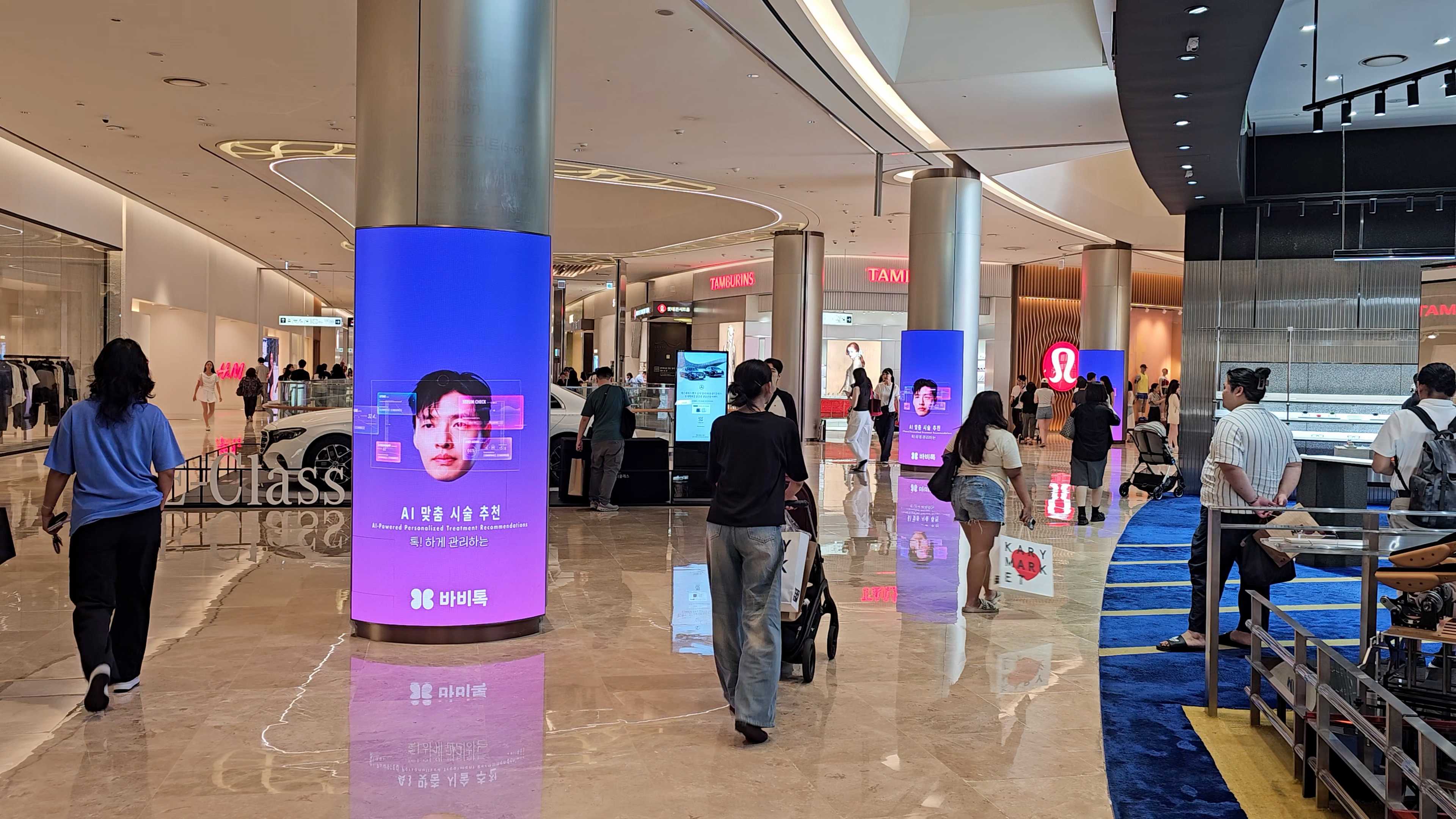 Shoppers walking past curved BABITALK digital columns in the main concourse of Lotte World Mall, Jamsil