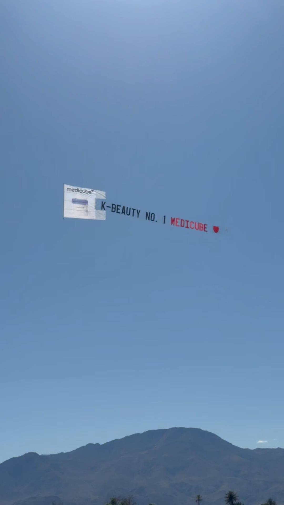 "K-BEAUTY NO. 1 MEDICUBE" aerial banner against a clear blue sky above the Coachella Valley