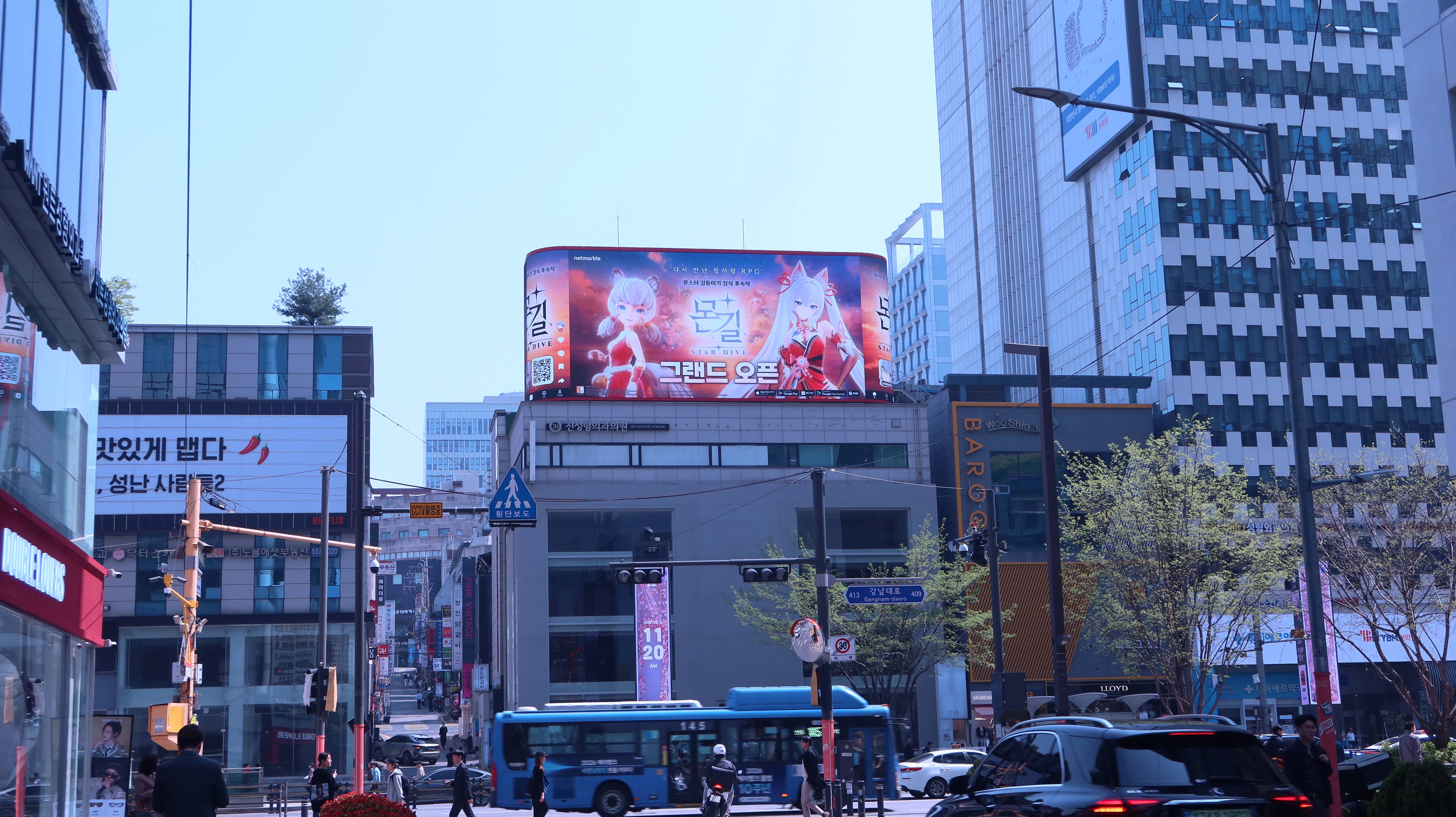 MONGIL: STAR DIVE grand open creative on a curved rooftop screen above Gangnam-daero as a city bus passes, Seoul