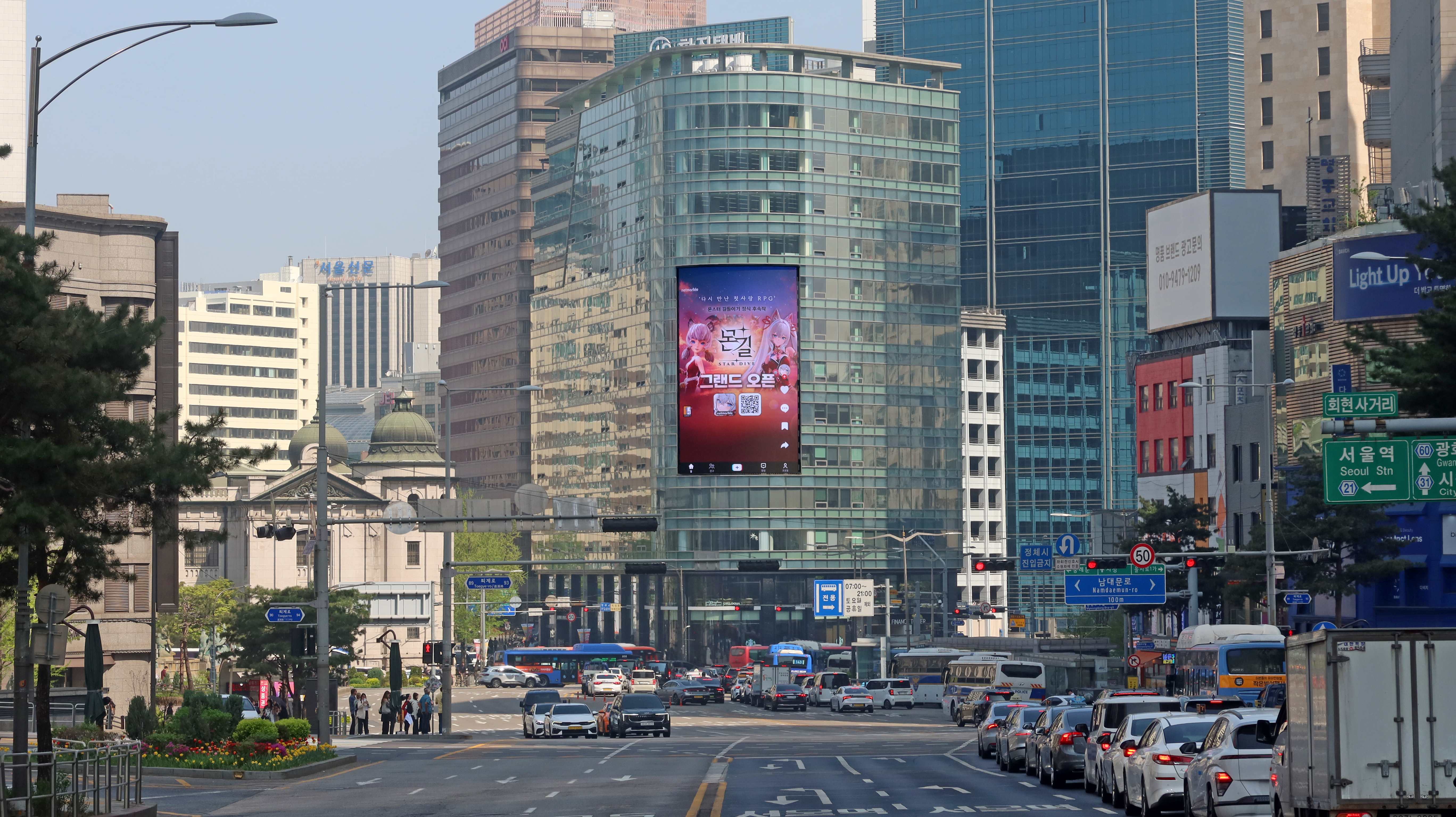 MONGIL: STAR DIVE grand open creative on the vertical screen of a glass tower above a wide central Seoul boulevard