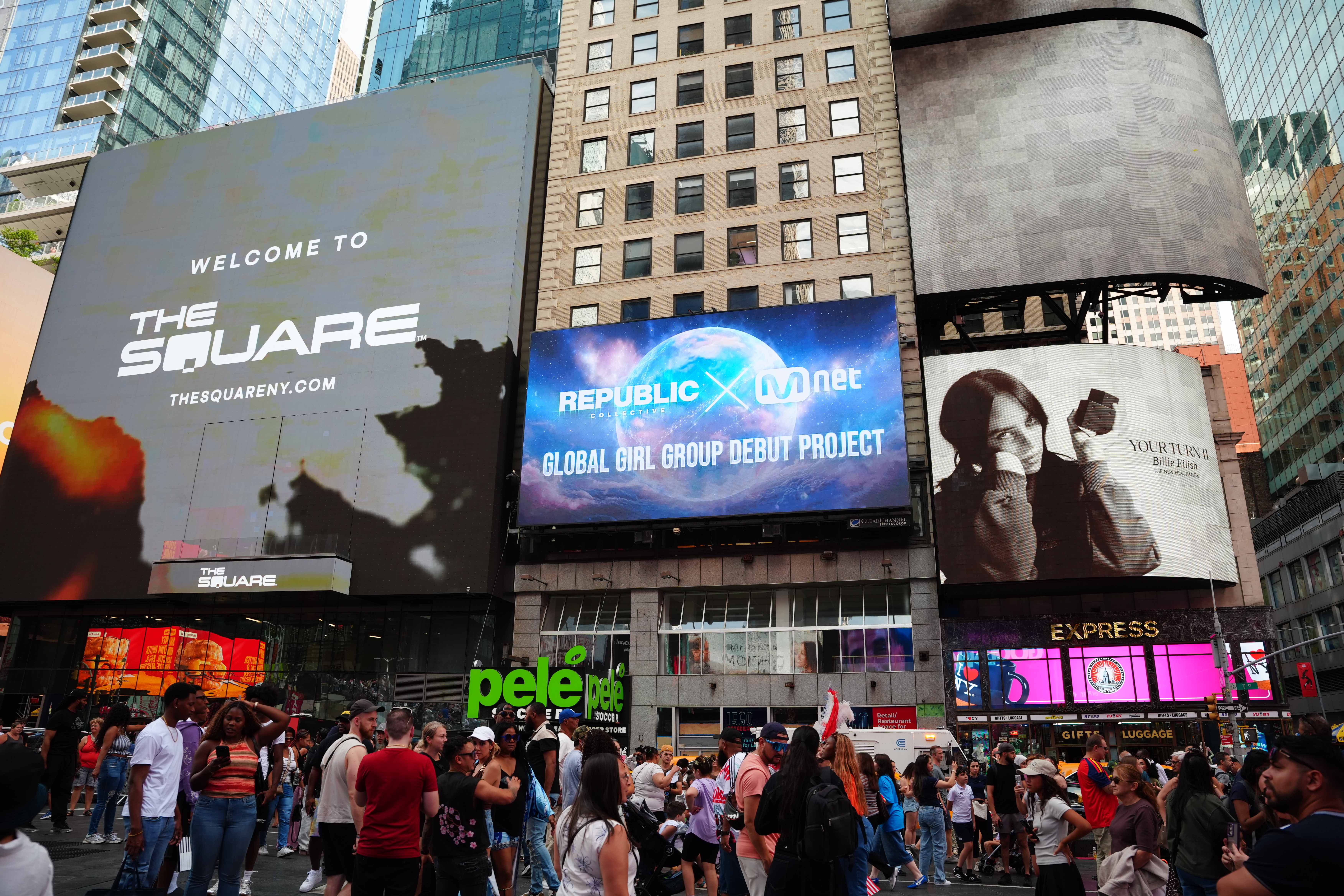Crowds in Times Square beneath the Republic Collective x Mnet Global Girl Group Debut Project screen